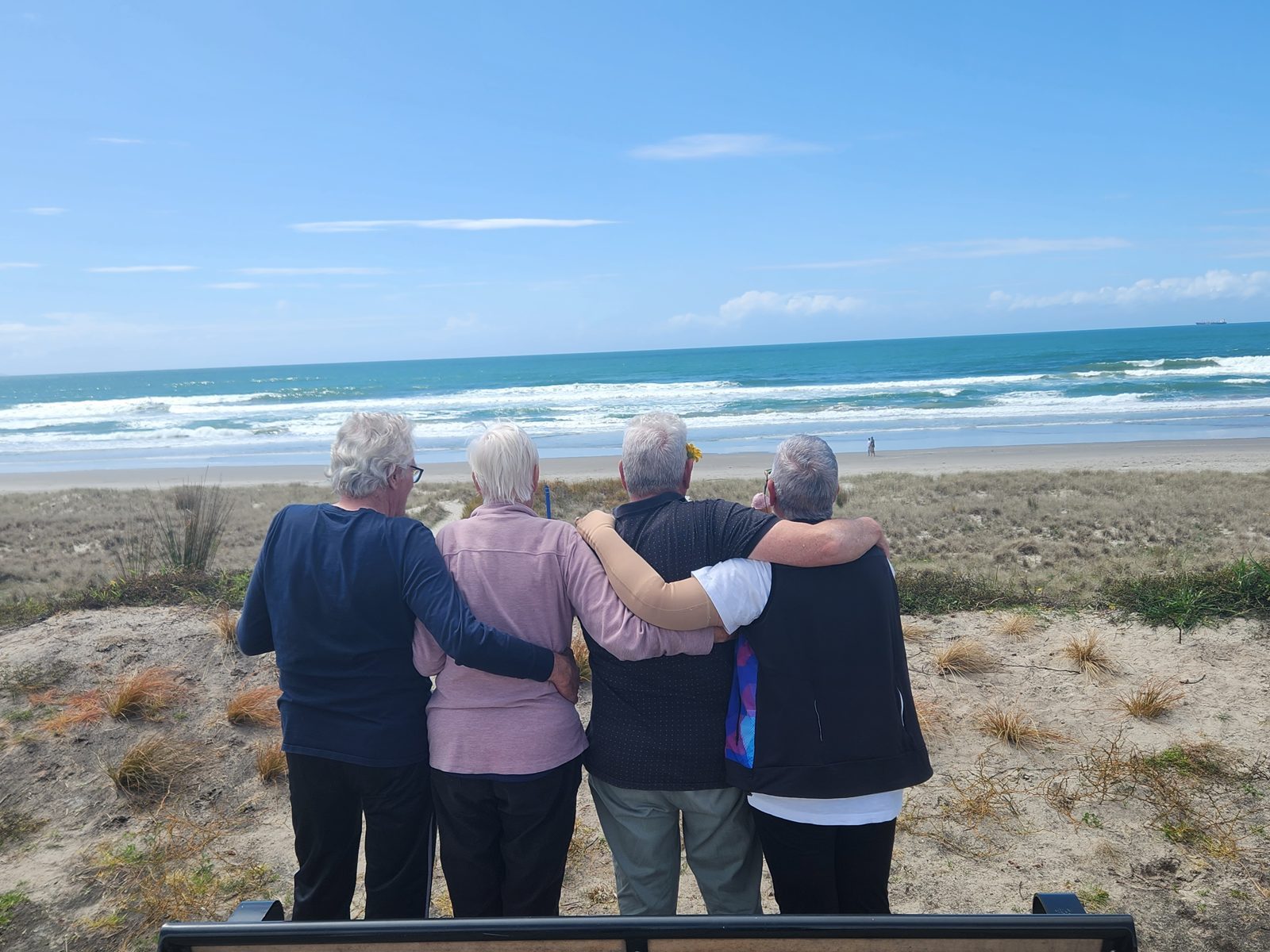 Four women arm in arm, looking out to sea.