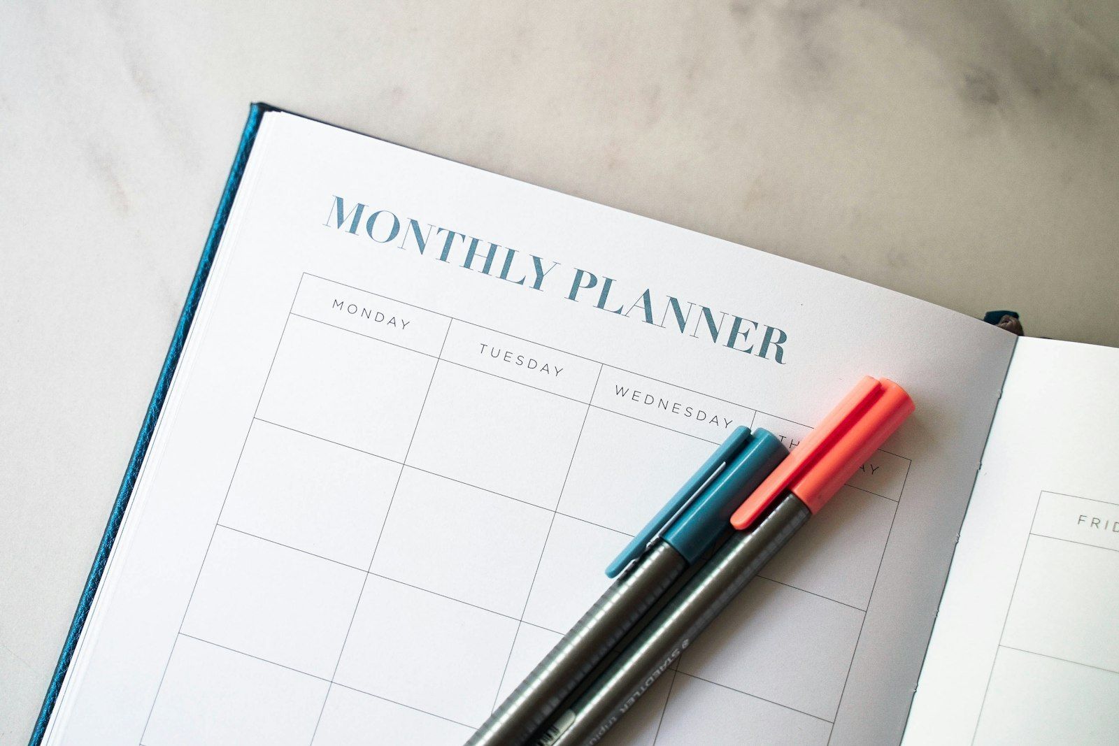 A desk with a planner, pens and a cup of coffee.