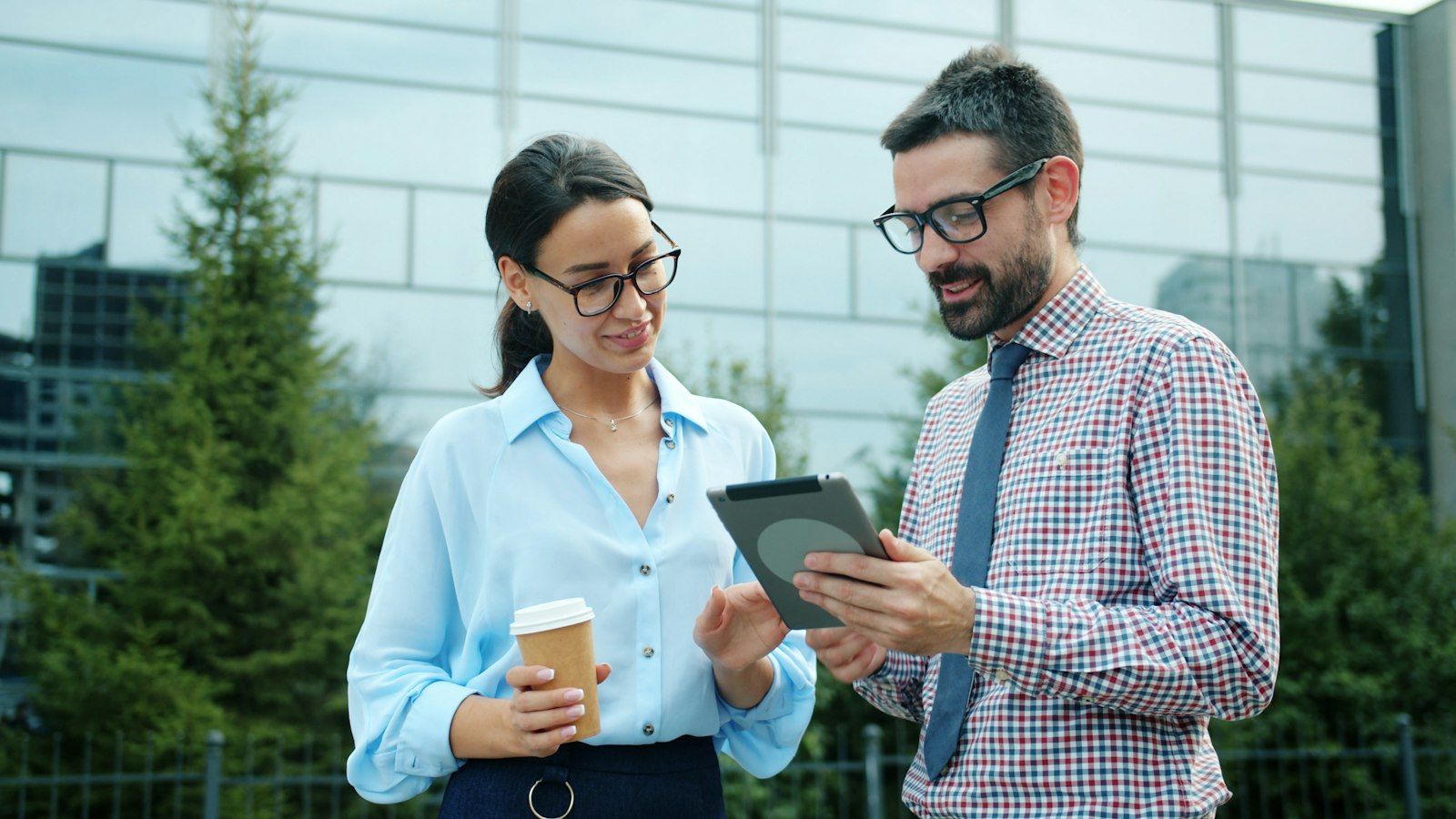 Two colleagues talking outdoors over a tablet.