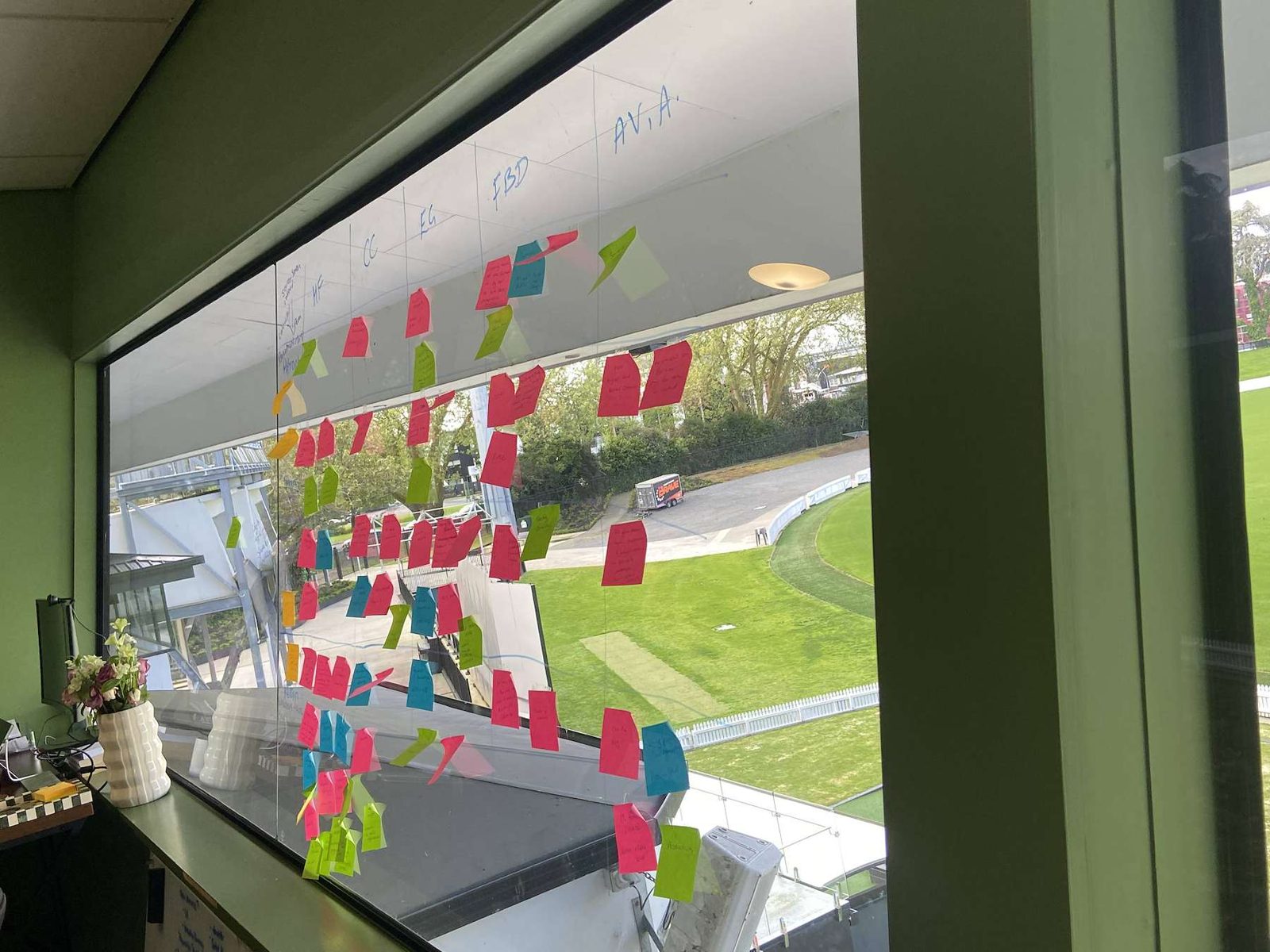 Sticky notes from a workshop on the office window, the cricket ground behind.